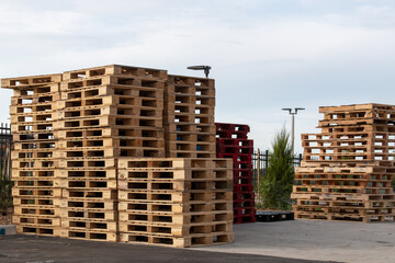 Multiple stacks of empty freight transport crates are piled high in a transport yard. The storage pallets are made of hardwood supports for forklift use. The skids are rectangular shape platforms.  