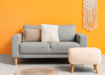 Cozy grey sofa with pillows and ottoman near orange wall