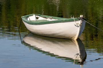 A small white colored wooden traditional dory or fishing vessel with green painted edging. The boat...