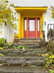 The entrance to a white wooden house with clapboard siding.The door is bright red with half glass...