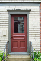 The exterior side entrance to a cream-colored wooden house. There's a closed red door with a...