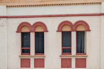 The exterior of a vintage white cement building with four tall closed glass windows. The trim around the windows is orange and yellow in color. Above the windows are arched decorative plaster tops. 