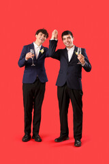 Married gay couple with glasses of champagne on red background