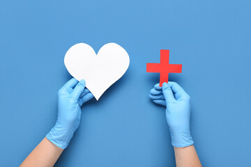 Doctor with paper heart and cross on blue background