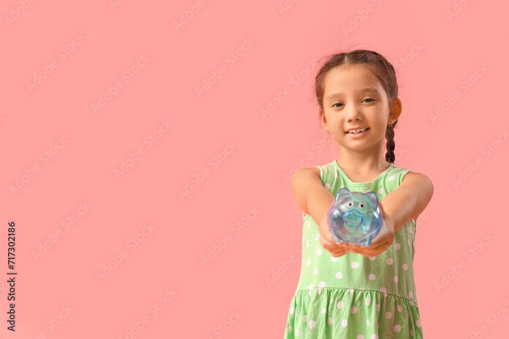 Wall mural Little girl with piggy bank on pink background