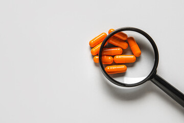 Magnifier with pills on grey background