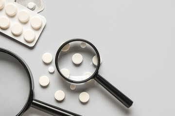 Magnifying glasses with pills on grey background