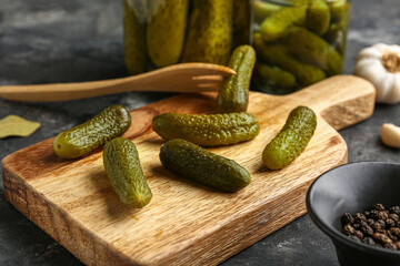 Wooden board with tasty pickled cucumbers and different spices on black background