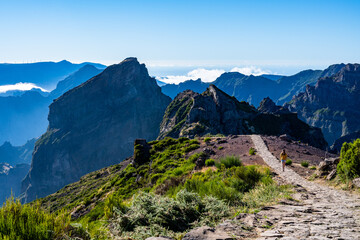 Female tourist walks along panoramic mountain trail and enjoys the picturesque view on a sunny summer day. Pico do Arieiro, Madeira Island, Portugal, Europe.