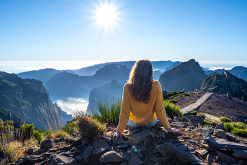 Female tourist sits on the summit of a mountain and enjoys the view of the landscape of a volcanic...