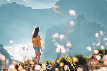Female tourist stands on the windy edge of a deep, cloud-covered valley and enjoys the breathtaking...