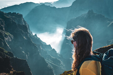 Portrait of a female backpacker looking down into a deep, cloud-covered valley and enjoying the...