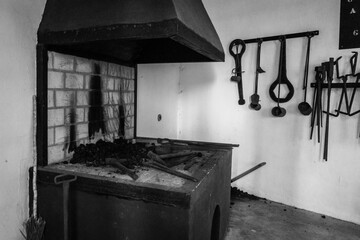 old metal forge with fire, chimney and tools placed on the wall.