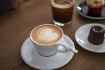Hot Latte espresso coffee with heart shape latte art in white ceramic cup serve with bakery on wooden table.  Morning breakfast.