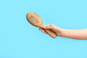 Female hand with wooden hairbrush on blue background.