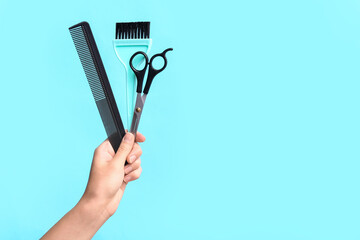 Female hand with different hairdresser's supplies on blue background.