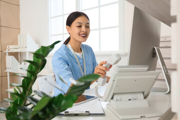 Obraz na płótnie Canvas Female Asian medical intern with telephone at reception in clinic