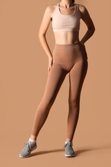 Sporty young woman in leggings on beige background