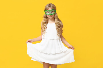 Happy little girl wearing carnival mask on yellow background