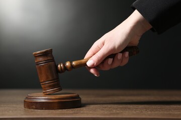 Judge striking mallet at wooden table against dark background, closeup