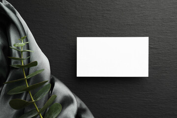 Blank business card and eucalyptus branch on black background, flat lay. Mockup for design