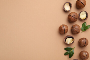 Tasty Macadamia nuts and green leaves on beige background, flat lay. Space for text