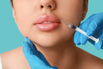 Young woman receiving lip injection on color background, closeup