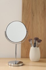 Mirror and makeup brushes on wooden dressing table in room