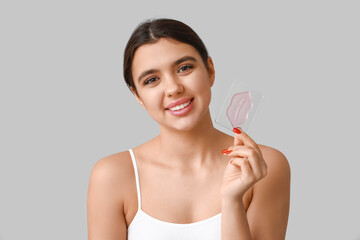 Happy young woman with lip mask on grey background
