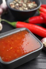 Spicy chili sauce in bowl on black wooden table, closeup