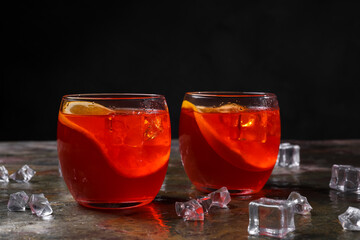 Aperol spritz cocktail, ice cubes and orange slices in glasses on grey textured table