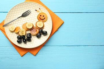 Creative serving for kids. Plate with cute caterpillar made of pancakes, grapes and banana on light...