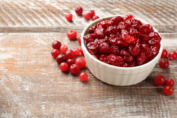 Tasty dried cranberries in bowl and fresh ones on rustic wooden table. Space for text