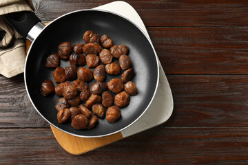 Roasted edible sweet chestnuts in frying pan on wooden table, top view. Space for text