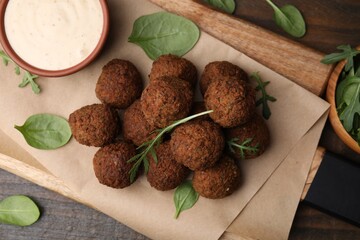 Delicious falafel balls, arugula, basil and sauce on wooden table, top view