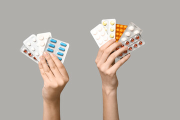 Female hands holding pills in blister packs on grey background