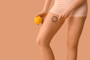 Beautiful young woman with cellulite problem, magnifier and orange on brown background