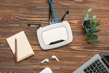 Modern wi-fi router with earphones and laptop on wooden background