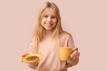 Little girl with tasty pancake and cup of tea on beige background