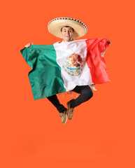 Mexican young man in sombrero hat with flag jumping on orange background