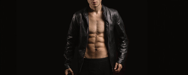 slender sexy man with a pumped up body in a dark leather jacket on a black background. Sports and healthy lifestyle.