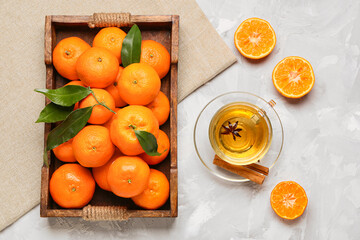 Wooden tray with sweet mandarins and cup of tea on grey background