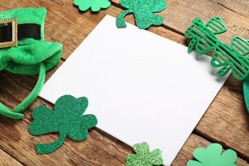 Blank card with plastic eyeglasses, leprechaun hat and paper clovers on wooden background. St....