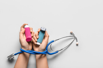 Child's hands with asthma inhalers and stethoscope on white background