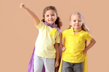 Cute little girls in superhero costume with yellow ribbons on brown background. Childhood cancer awareness concept