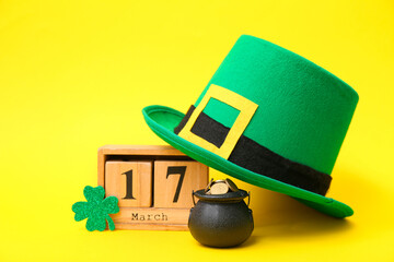 Pot with golden coins, calendar and leprechaun hat on yellow background. St. Patrick's Day...