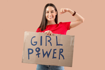 Beautiful young happy woman holding paper with text GIRL POWER and showing muscles on beige background. Women history month