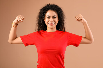 Beautiful young happy African-American woman showing muscles on beige background. Women history...