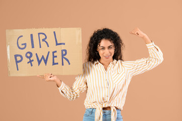 Beautiful young happy African-American woman holding paper with text GIRL POWER and showing muscles...