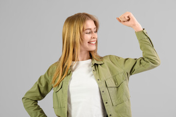 Beautiful young happy woman showing muscles on grey background. Women history month